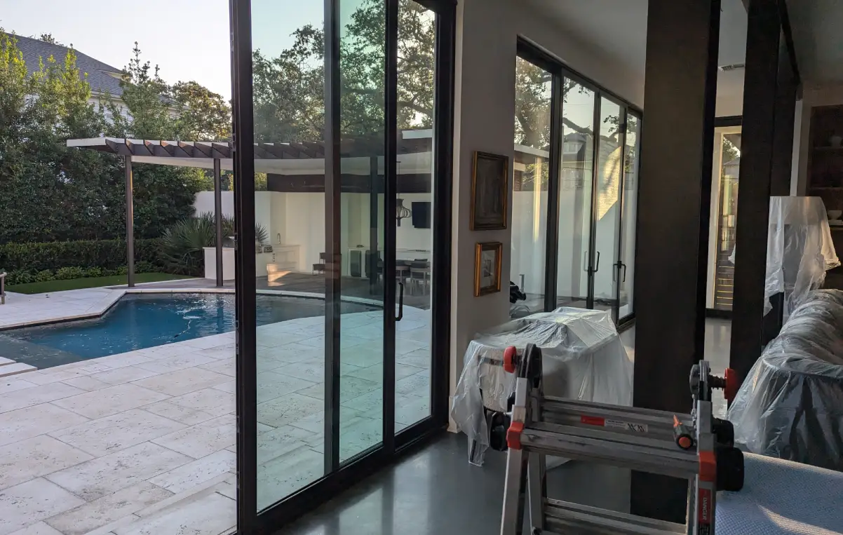 A modern home interior with a view of a pool area, featuring large glass doors, a ladder, and furniture covered in protective plastic